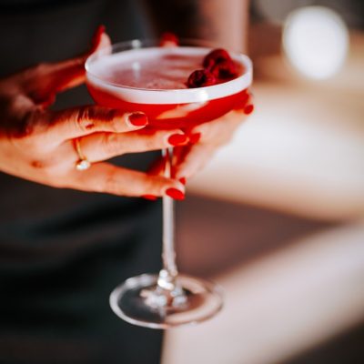 Elegant,Woman,Holding,A,Cocktail,Garnished,With,Raspberries,At,A